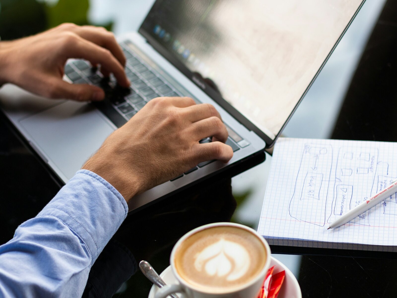 Hands testing software on a laptop with a notepad